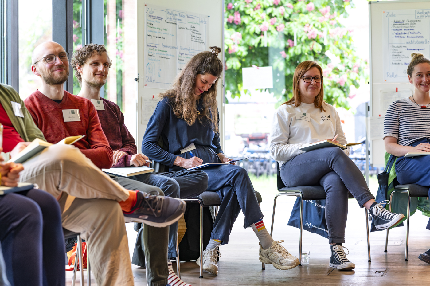Fotografie von Menschen, die auf Stühlen sitzen, in Bücher schreiben oder aufmerksam zuhören.