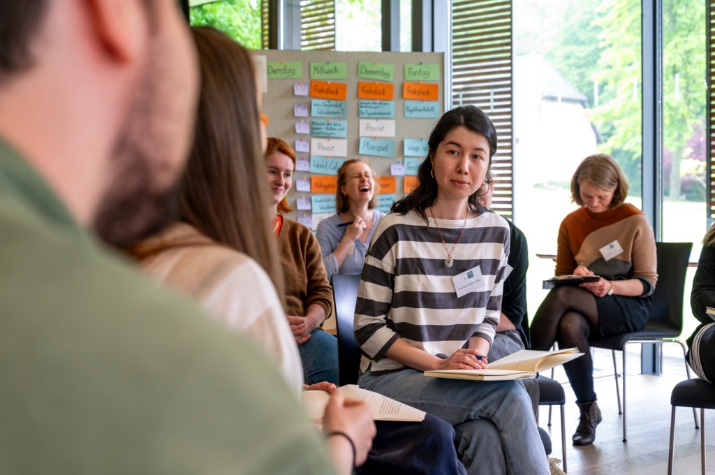 Foto einer Frau, die in einer Gruppe sitzt und aufmerksam zuhört.