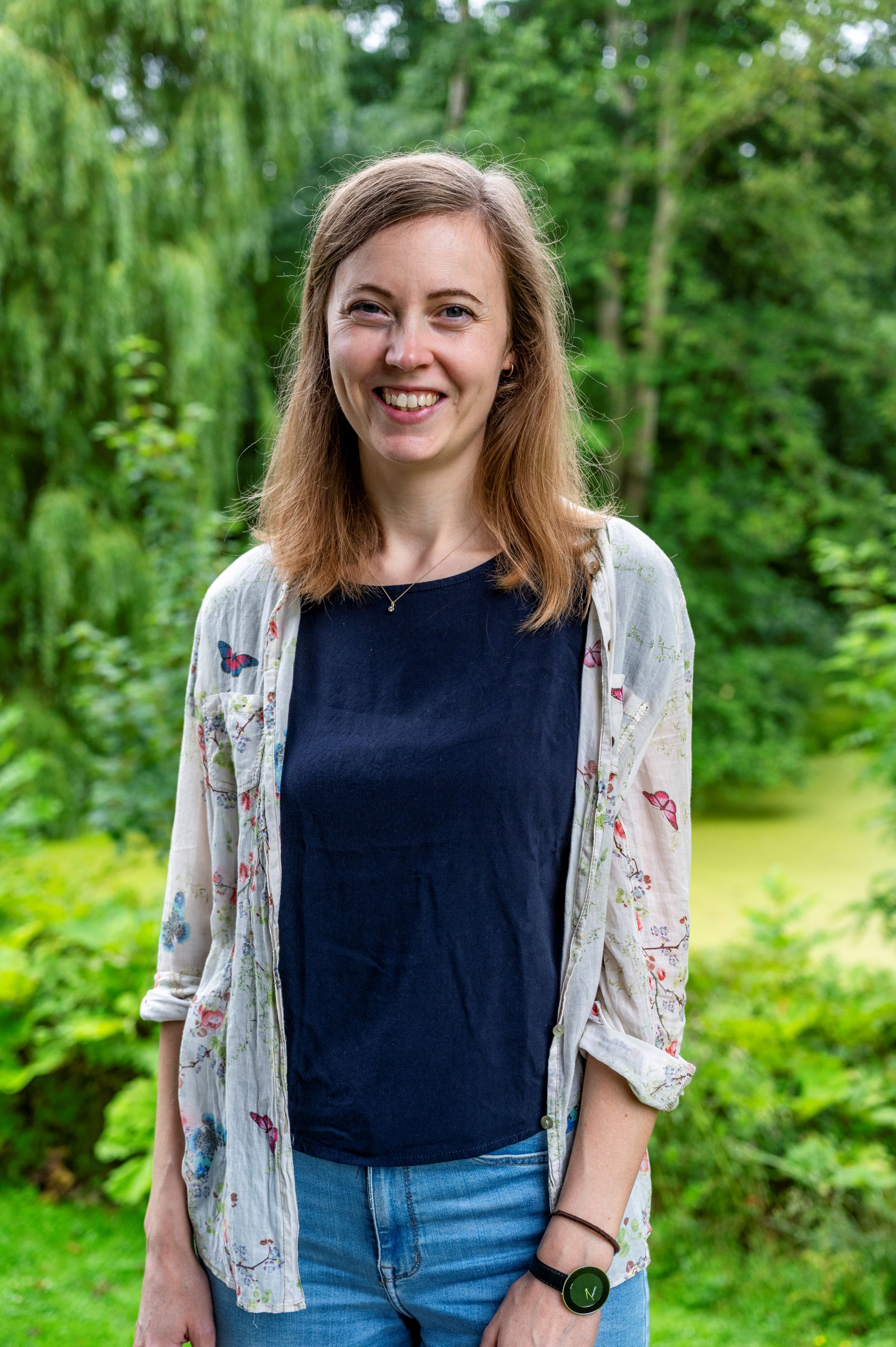 Foto einer Frau mit blauen Shirt, darüber ein geblümtes Hemd.