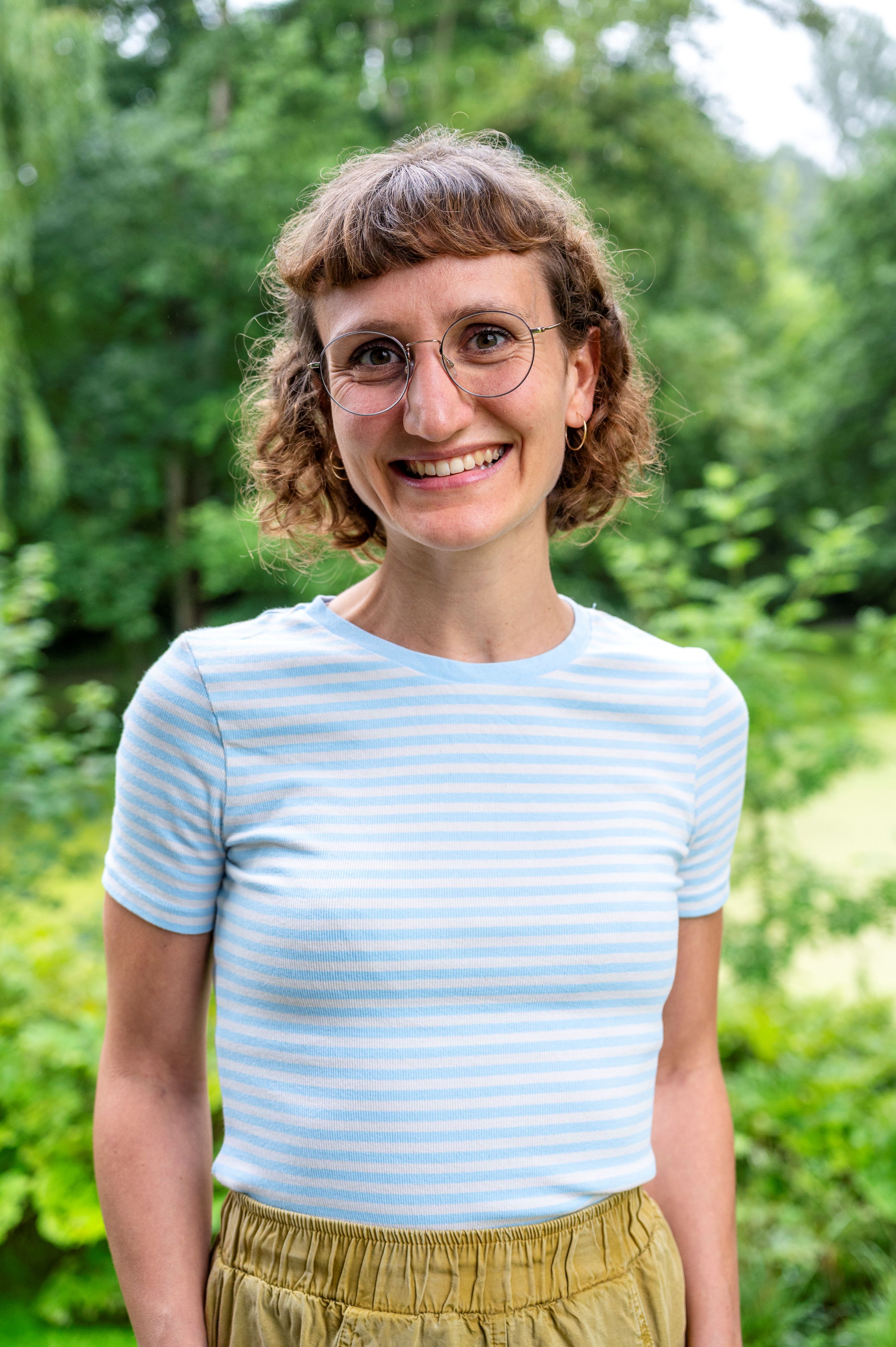 Foto einer Frau mit kurzen Haaren und hellblau gestreiften T-Shirt.