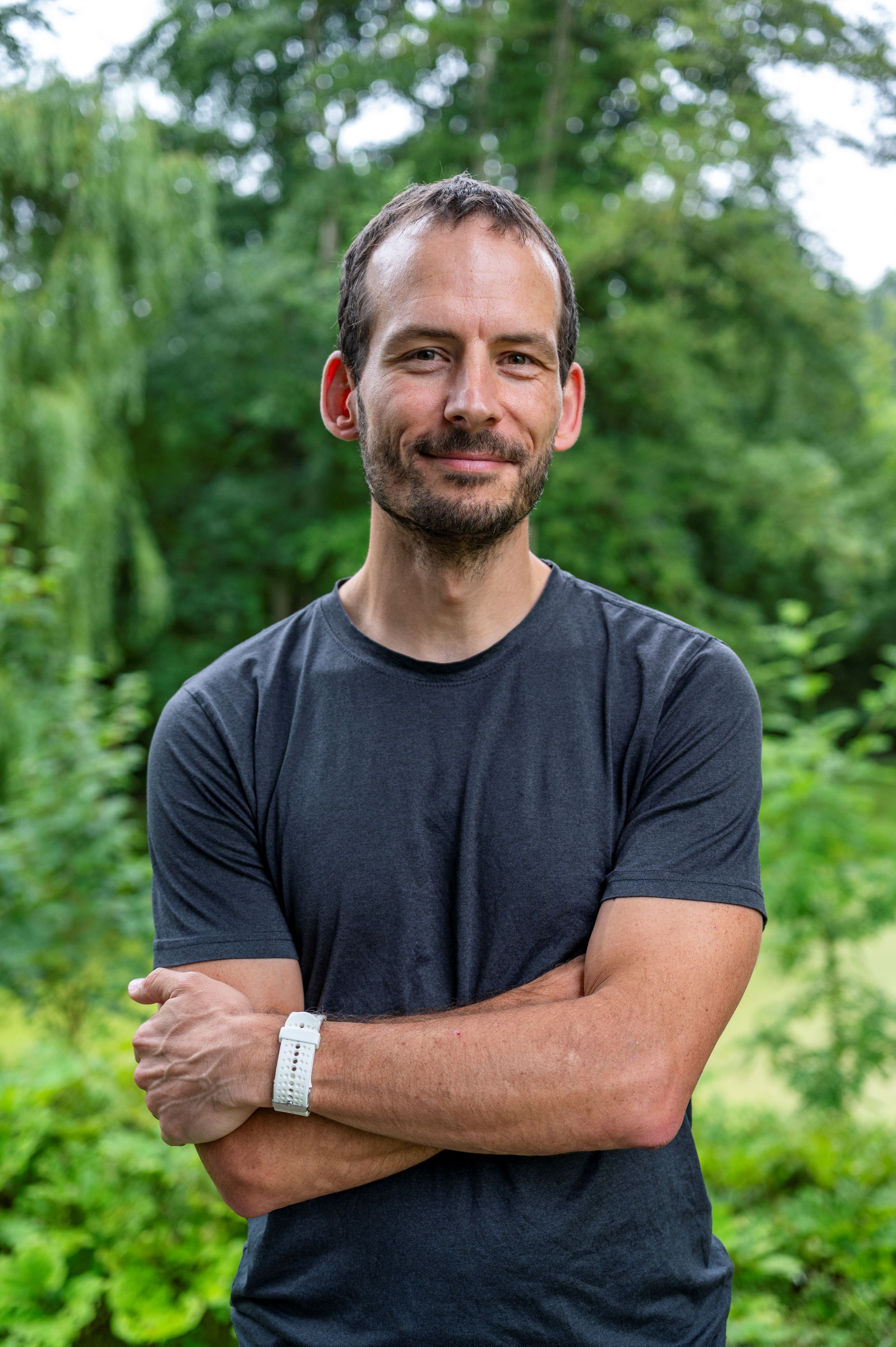 Foto eines Mannes in grauen T-Shirt, der die Arme verschränkt hält.
