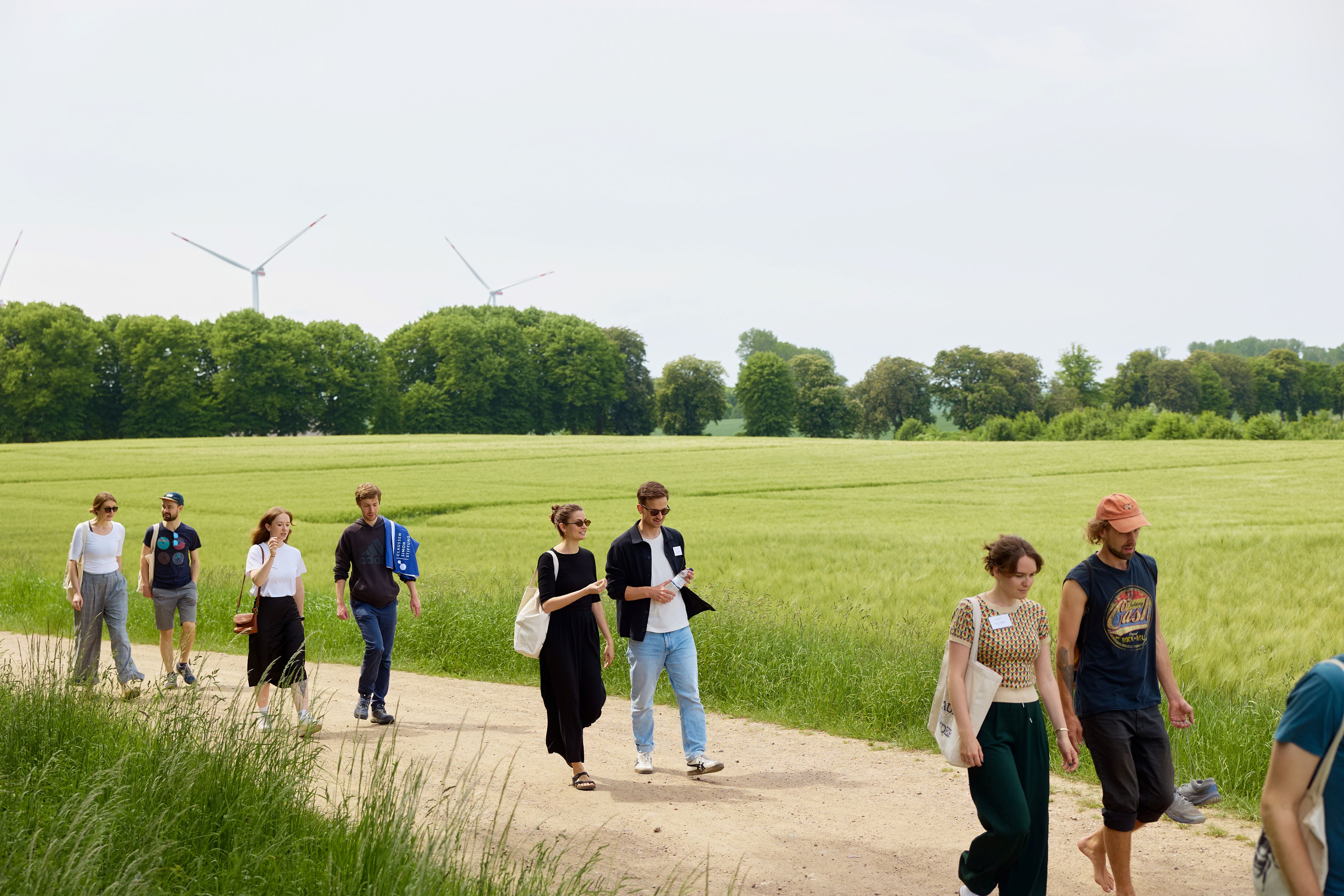 Personen spazieren in zweier Gruppen an einem Getreidefeld entlang